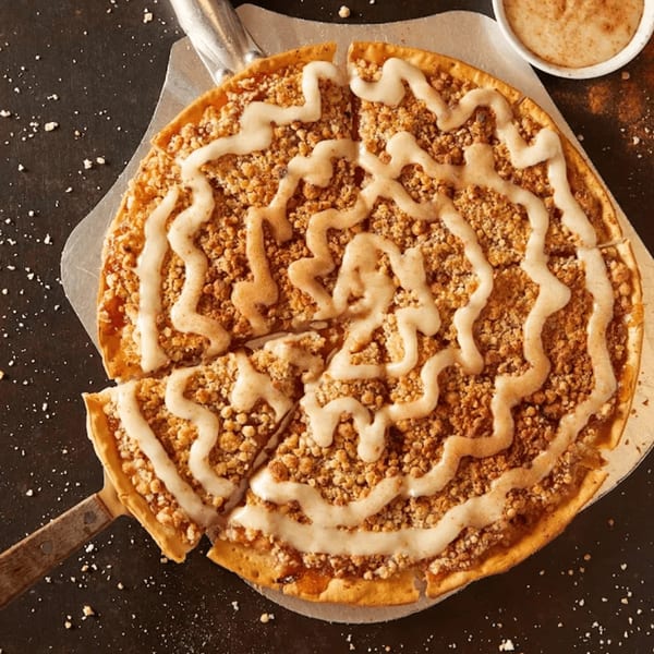 Plaza Pizza's apple crumble dessert pizza with icing drizzle, a slice removed.