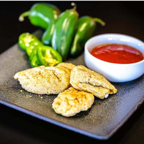 Plaza Pizza's breaded jalapeño poppers with a side of red dipping sauce and fresh jalapeños.