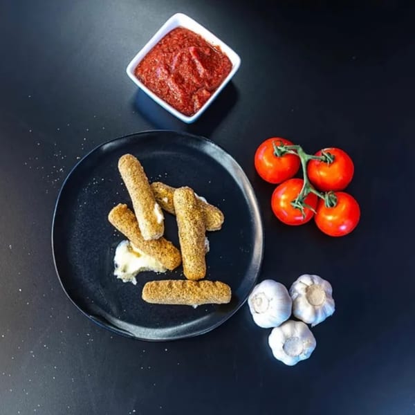 Plaza Pizza mozzarella sticks with marinara sauce, tomatoes, and garlic on a dark surface.