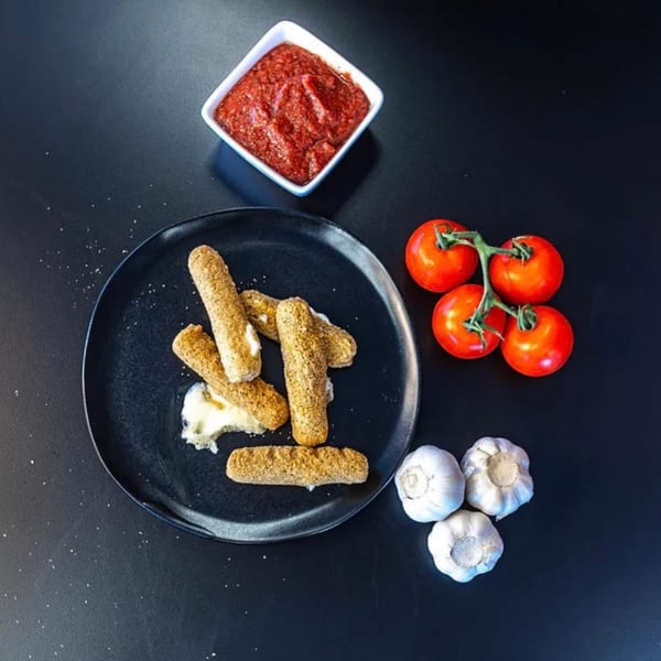 Plaza Pizza mozzarella sticks with marinara sauce, fresh tomatoes, and garlic on a dark surface.