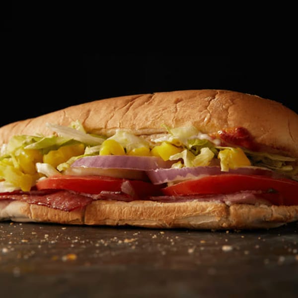A large, fresh sub sandwich filled with salami, tomatoes, red onions, lettuce, and peppers.