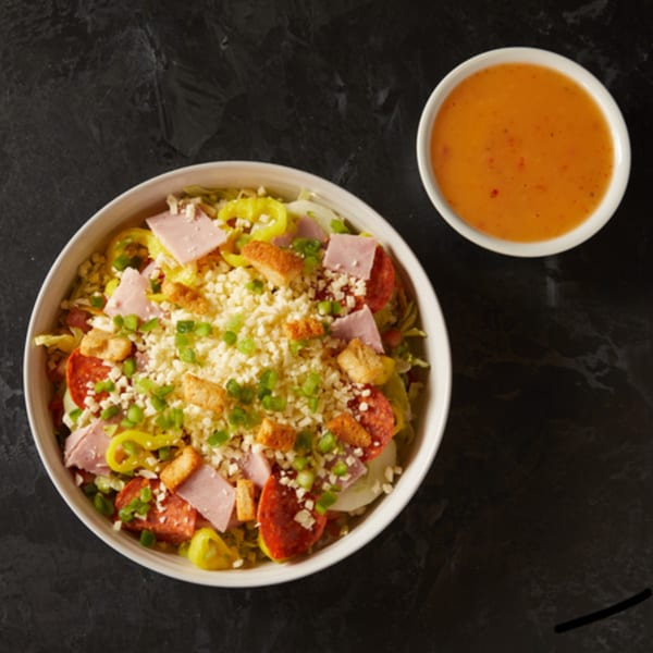 Plaza Pizza's antipasto salad with ham, pepperoni, cheese, croutons, and dressing on a dark surface.