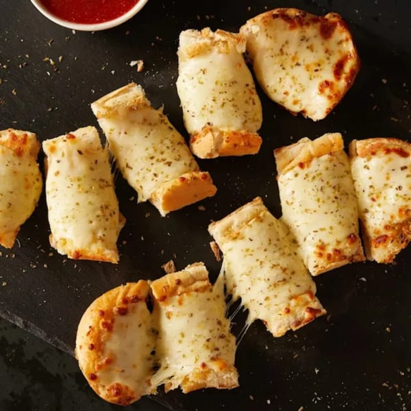 Cheesy breadsticks with herbs and a side of marinara sauce on a dark surface.