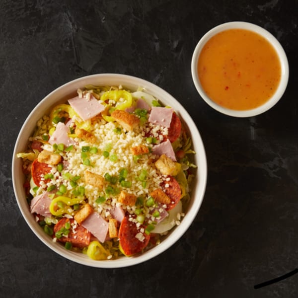 Plaza Pizza's antipasto salad with ham, pepperoni, cheese, croutons, and dressing on a dark background.