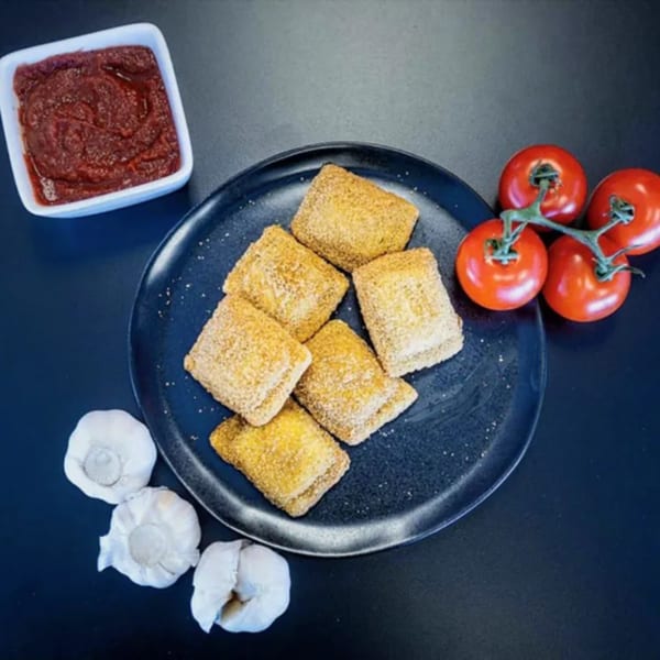 Plaza Pizza's golden-brown pizza bites on a dark plate, with a side of marinara, garlic, and tomatoes.