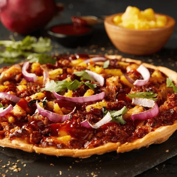 Plaza Pizza's BBQ chicken pizza with red onions, pineapple, and cilantro on a dark surface.