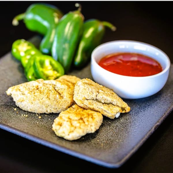 Plaza Pizza's breaded jalapeno poppers with a side of red dipping sauce and fresh jalapenos.