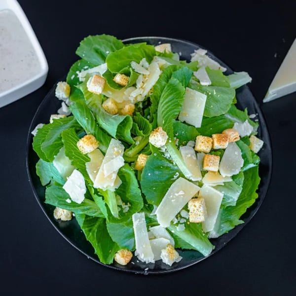 A fresh Caesar salad from Plaza Pizza, with crisp romaine, croutons, and Parmesan cheese.