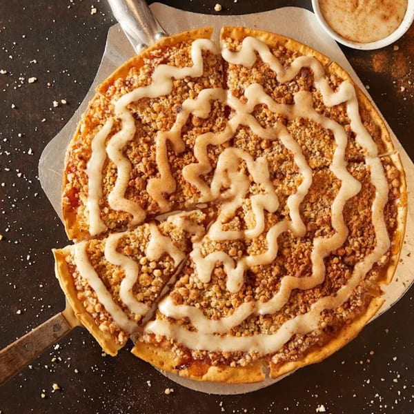 Plaza Pizza's apple crumble dessert pizza with icing drizzle and a serving spatula.