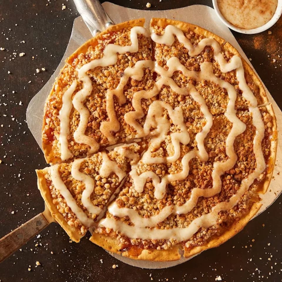 Plaza Pizza's apple crumble dessert pizza with icing drizzle and a serving spatula.